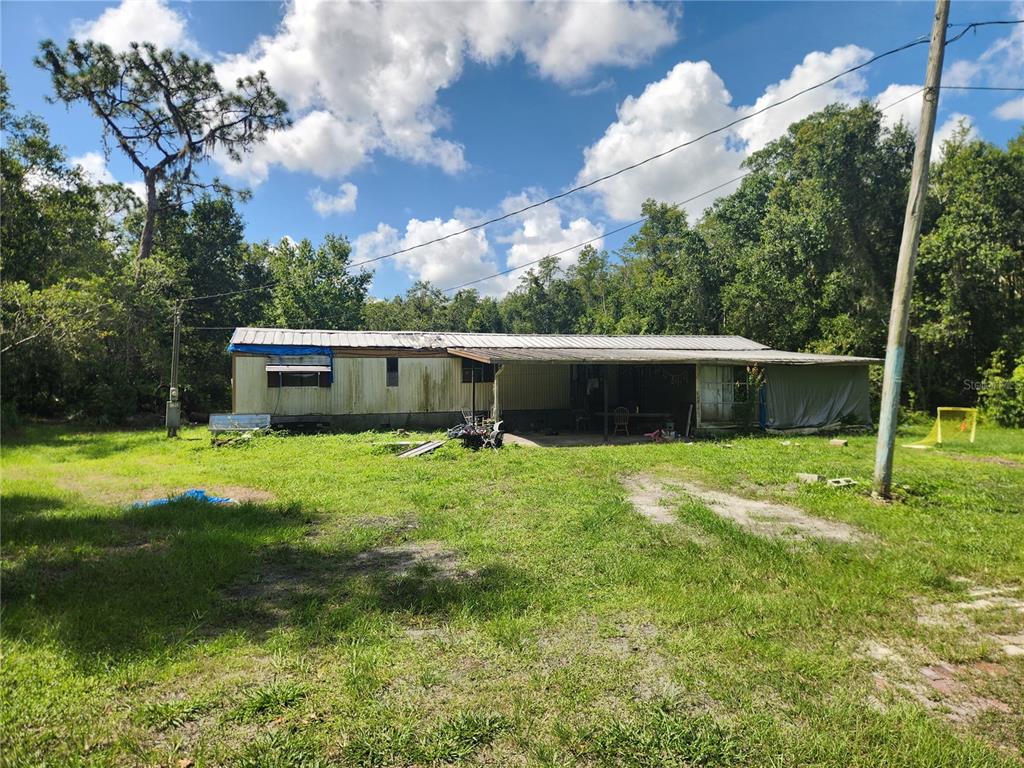 An exterior view of a weathered mobile home with a metal roof and attached carport — 326 CREEKWOOD RUN, LAKELAND, FL