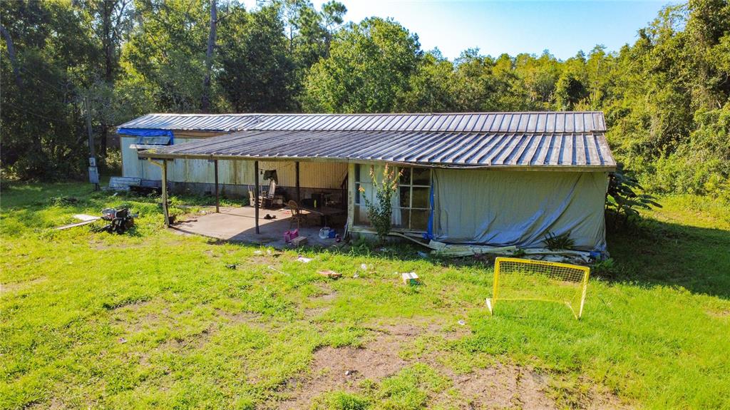 An exterior view of a weathered mobile home with a large metal-roofed porch and yard — 326 CREEKWOOD RUN, LAKELAND, FL