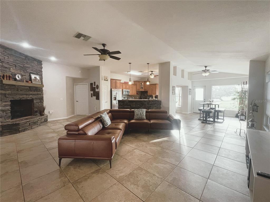 A spacious open-concept living room features a stone fireplace, tile flooring, and a leather sectional — 521 W HILLWOOD PATH, BEVERLY HILLS, FL