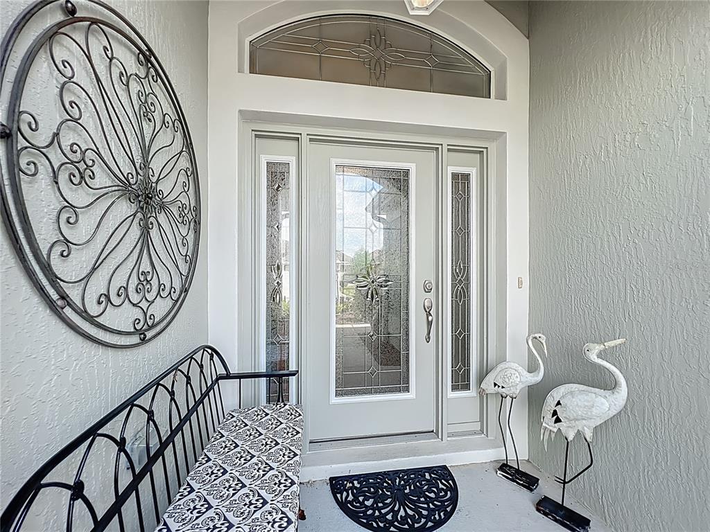 A front entryway features a decorative glass door, a metal bench, and two crane statues — 2875 RAIN LILY LOOP, THE VILLAGES, FL