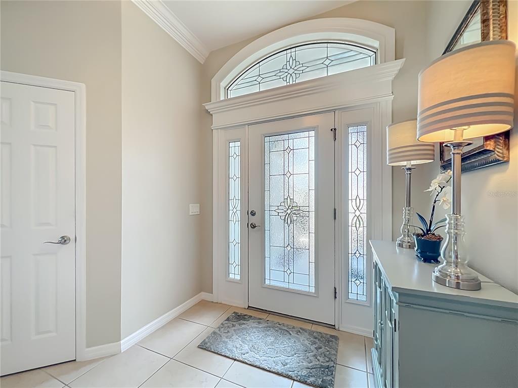 A bright entryway features a white front door with glass panels and a transom window — 2875 RAIN LILY LOOP, THE VILLAGES, FL