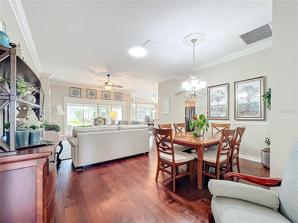 A dining area and living room feature hardwood floors, neutral walls, and a chandelier — 2875 RAIN LILY LOOP, THE VILLAGES, FL