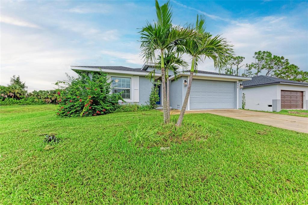 A single-story house with a gray exterior, a two-car garage, and palm trees in the yard — 320 ALBATROSS ROAD, ROTONDA WEST, FL