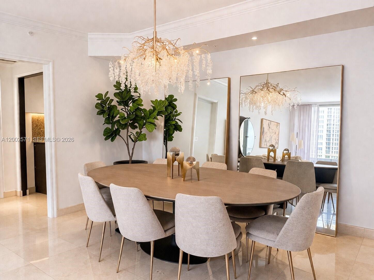 A dining room features an oval wooden table, upholstered chairs, and a large crystal chandelier — 848 Brickell Key Dr # 905, Miami FL 33131, MIAMI, FL