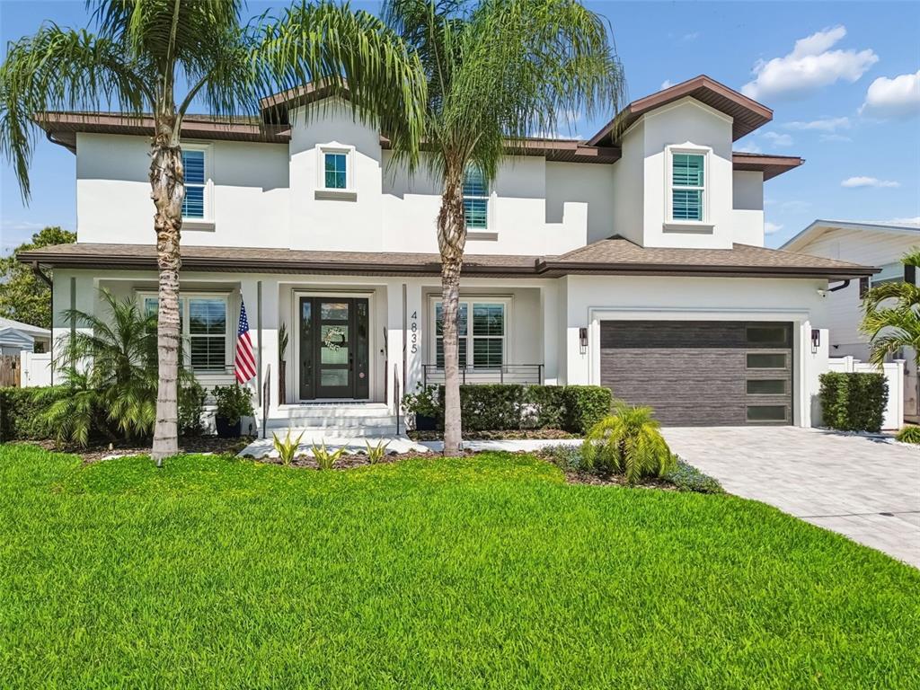 A two-story white house with a dark garage door, palm trees, and a front lawn — 4835 W BAY VILLA AVENUE, TAMPA, FL