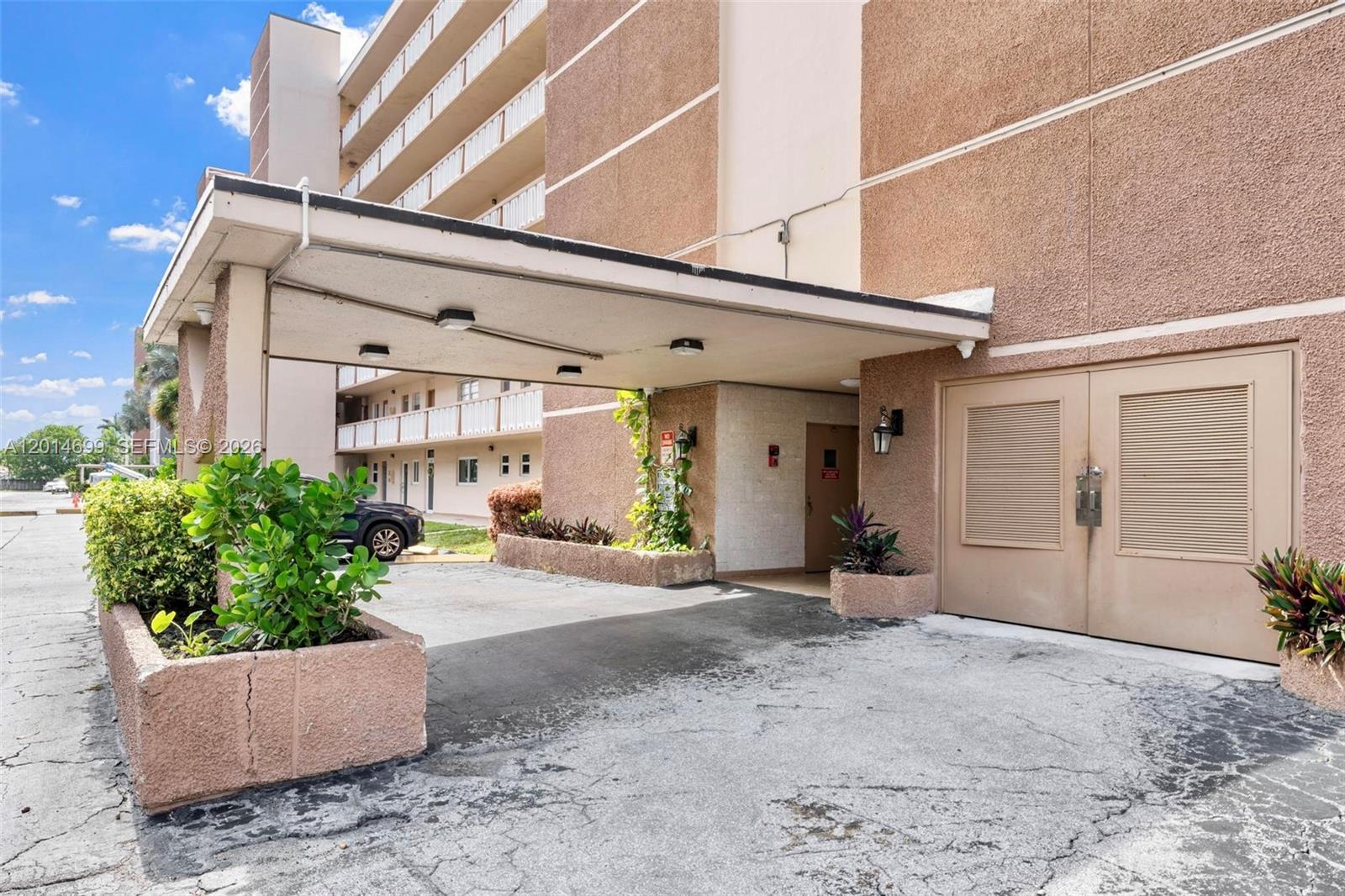 The exterior of a multi-story apartment building features a covered drop-off area and planters — 609 NE 14th Ave # 405, Hallandale Beach FL 33009, HALLANDALE BEACH, FL