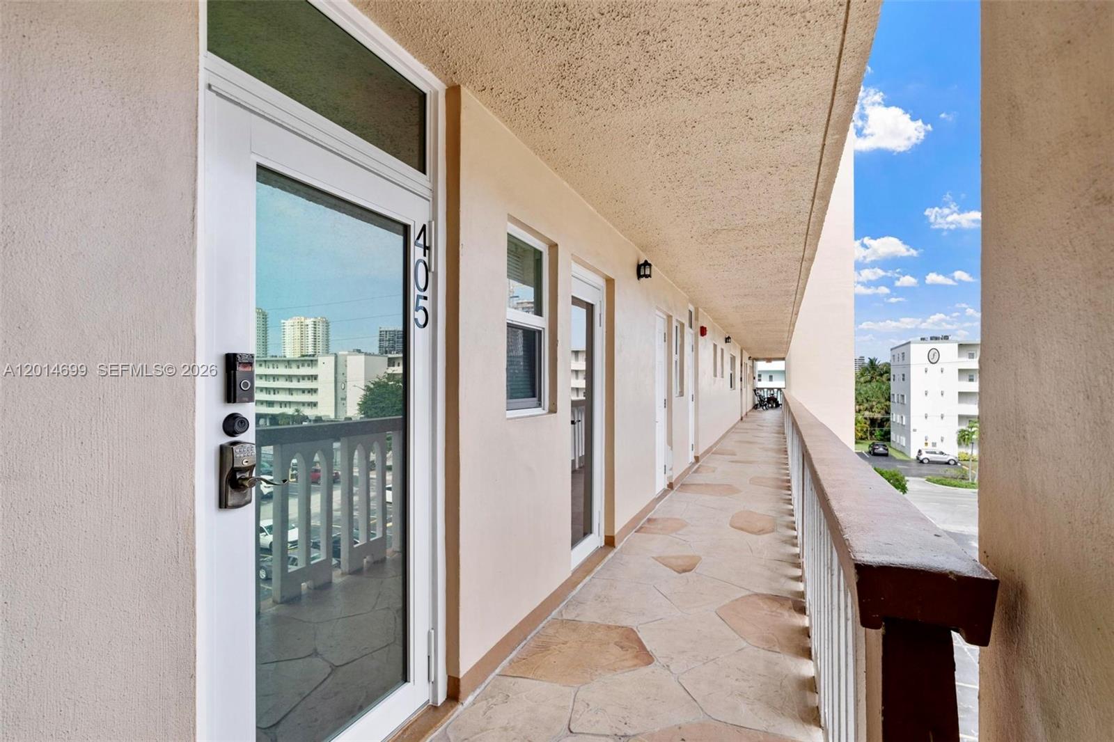 An outdoor apartment building walkway features a stone-tiled floor and a numbered glass door — 609 NE 14th Ave # 405, Hallandale Beach FL 33009, HALLANDALE BEACH, FL