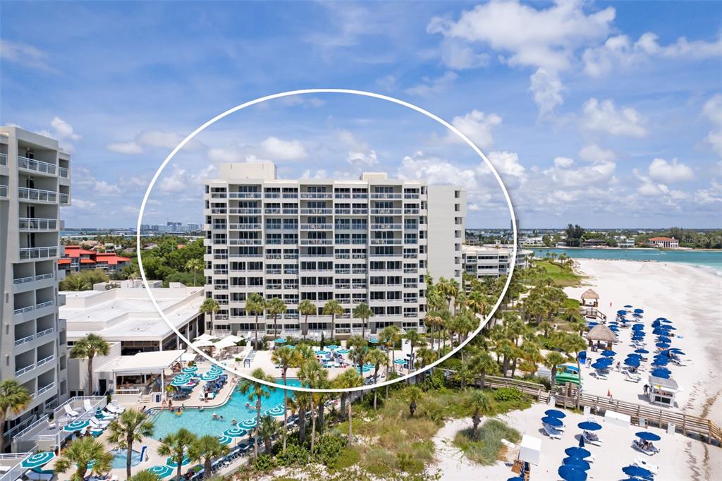 An aerial view shows a multi-story beachfront condominium building with a pool and palm trees — 210 SANDS POINT ROAD UNIT 2402, LONGBOAT KEY, FL