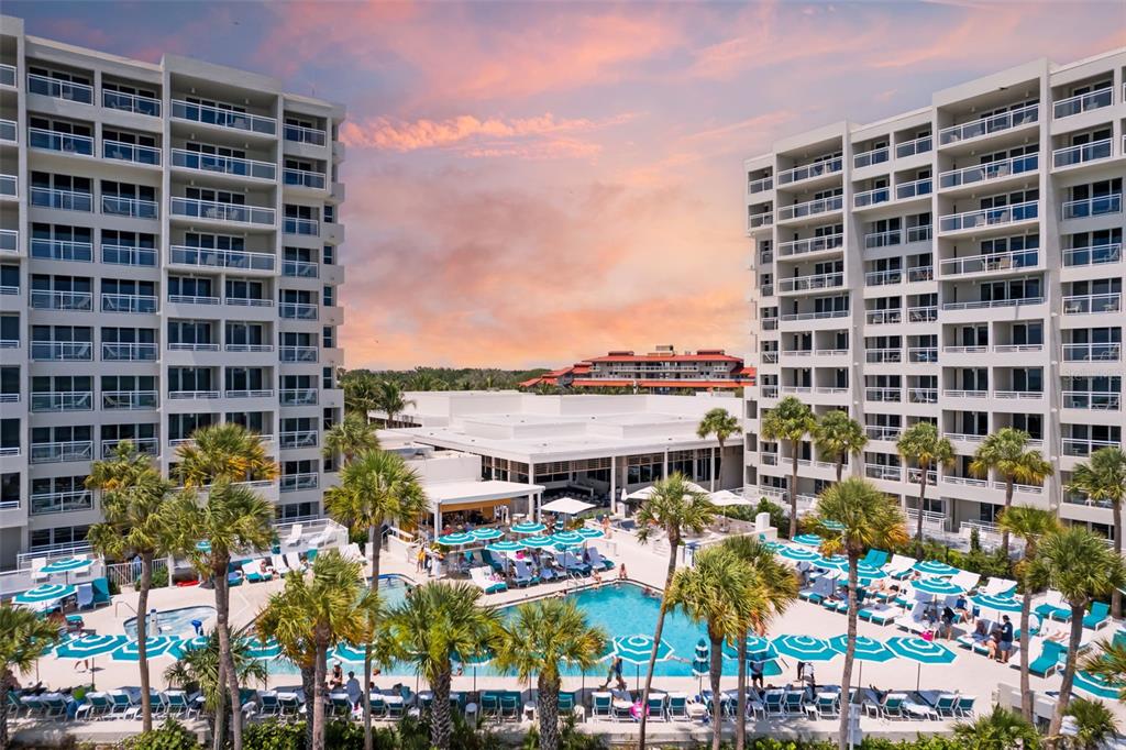 An aerial view shows two hotel buildings flanking a swimming pool with lounge chairs and umbrellas — 210 SANDS POINT ROAD UNIT 2402, LONGBOAT KEY, FL