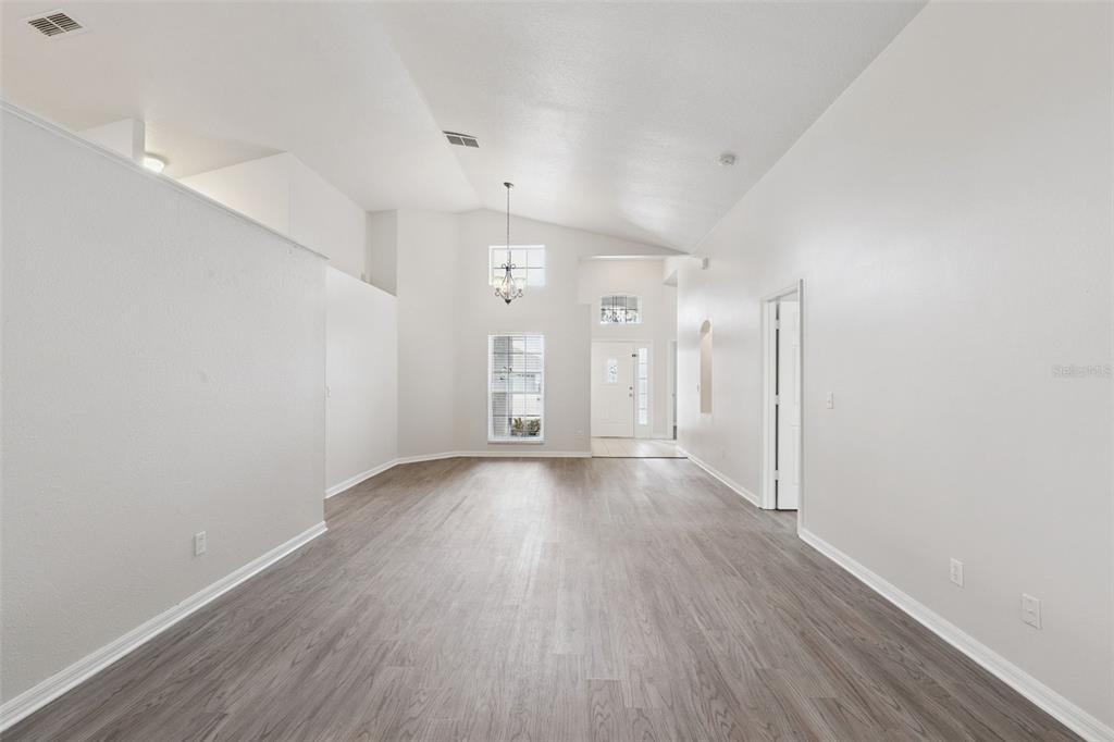 An empty room with vaulted ceilings, light gray walls, and wood-look flooring — 5483 GLEN OAK PLACE, SANFORD, FL