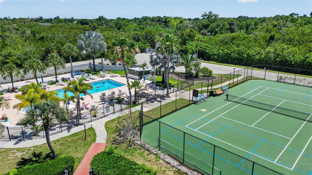 An aerial view shows a swimming pool and a tennis court surrounded by palm trees — 25188 MARION AVENUE UNIT E208, PUNTA GORDA, FL