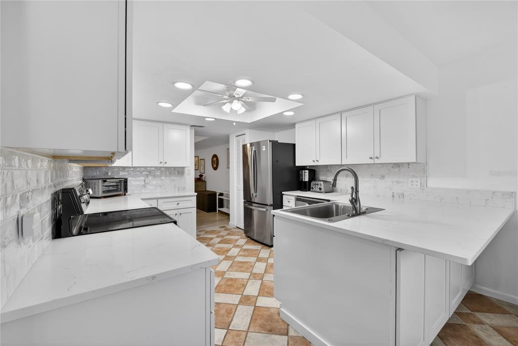A white kitchen features quartz countertops, stainless steel appliances, and a tiled floor — 25188 MARION AVENUE UNIT E208, PUNTA GORDA, FL