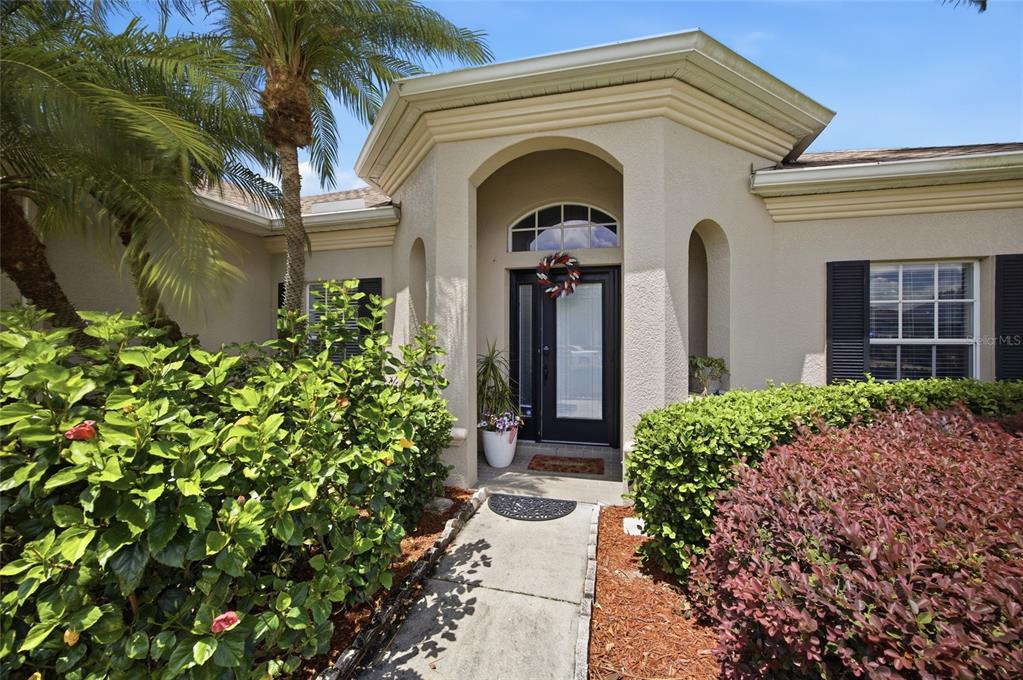 A beige house exterior features a covered entryway with a glass door and palm trees — 4369 85TH AVENUE CIRCLE E, PARRISH, FL