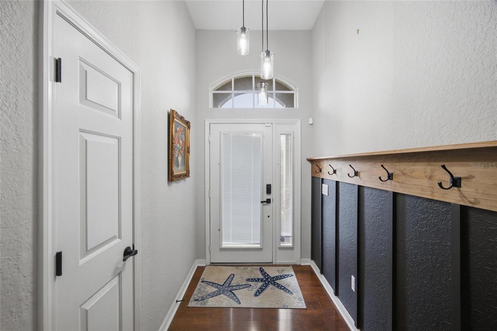 An entryway features a dark wood-paneled wall with coat hooks, a front door, and lighting — 4369 85TH AVENUE CIRCLE E, PARRISH, FL