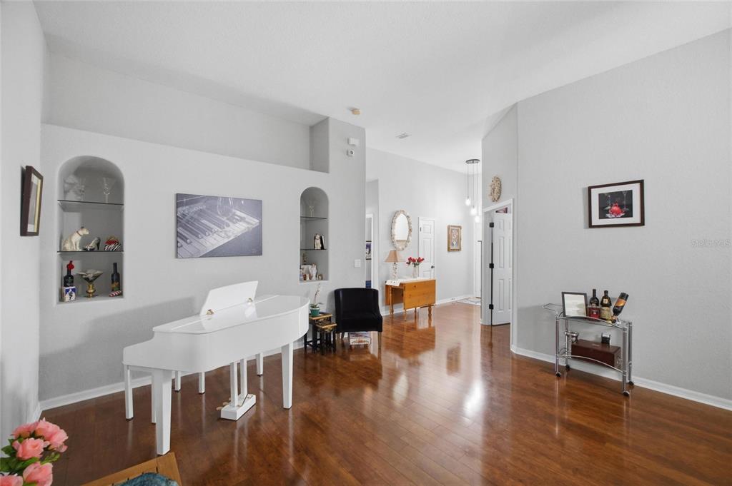 A white grand piano sits in a living room with hardwood floors and arched niches — 4369 85TH AVENUE CIRCLE E, PARRISH, FL