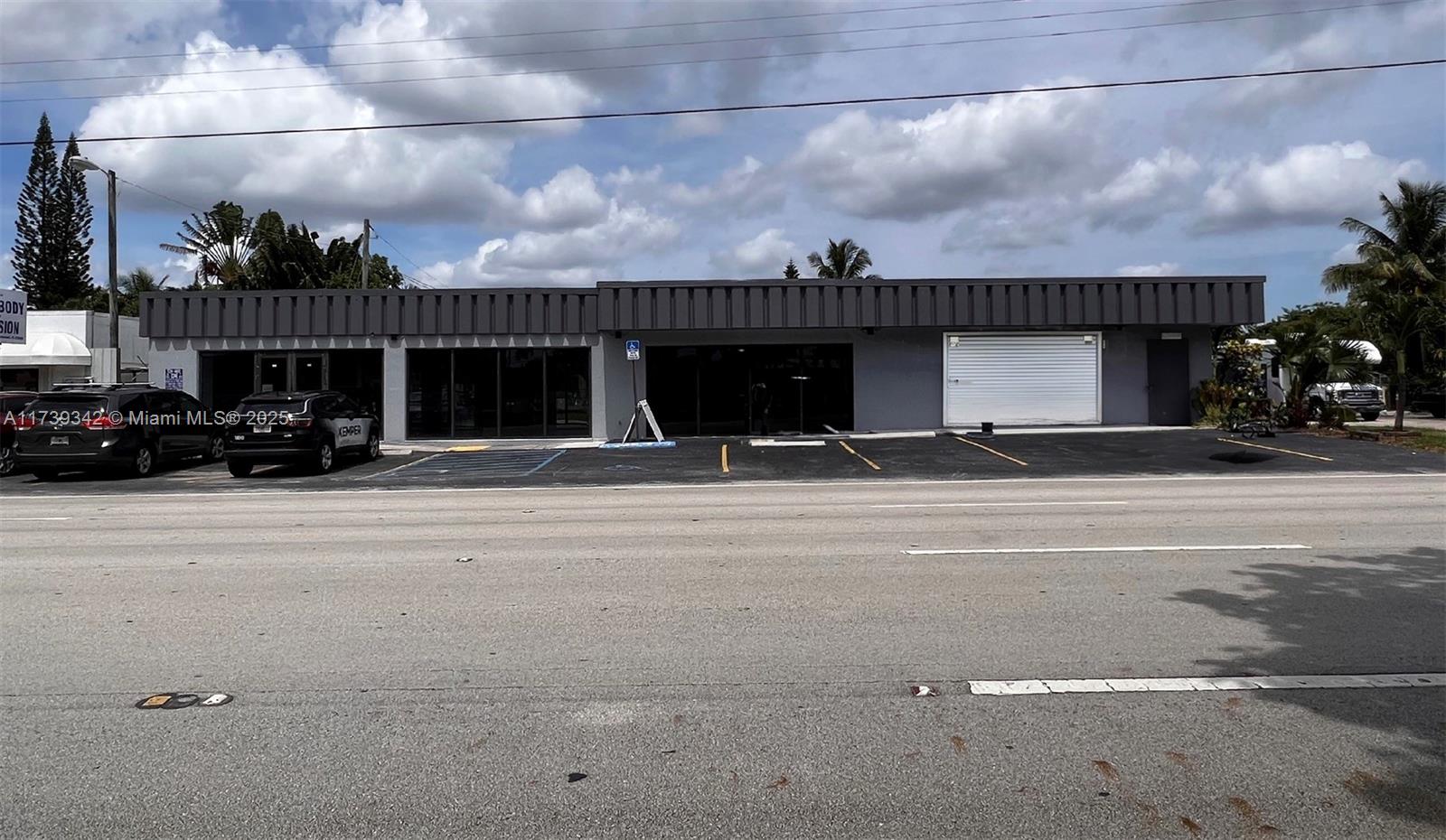 A single-story commercial building with a gray facade, glass storefronts, and a roll-up garage door — 1100 S Dixie Hwy, Hollywood FL 33020, HOLLYWOOD, FL
