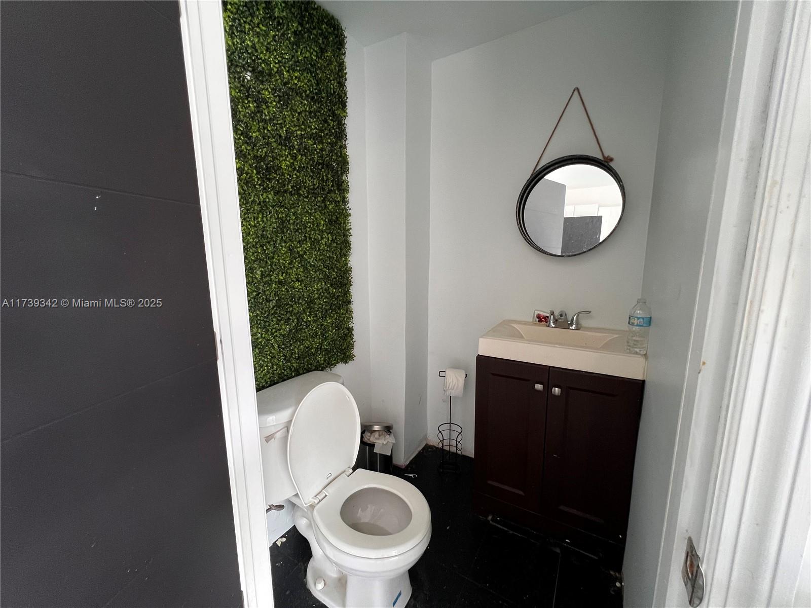 A small bathroom features a toilet, a dark wood vanity, and a green wall accent — 1100 S Dixie Hwy, Hollywood FL 33020, HOLLYWOOD, FL
