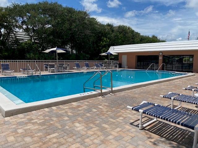 A rectangular outdoor swimming pool with lounge chairs on a paved deck near a building — 4150 S ATLANTIC AVENUE UNIT 121B, NEW SMYRNA BEACH, FL