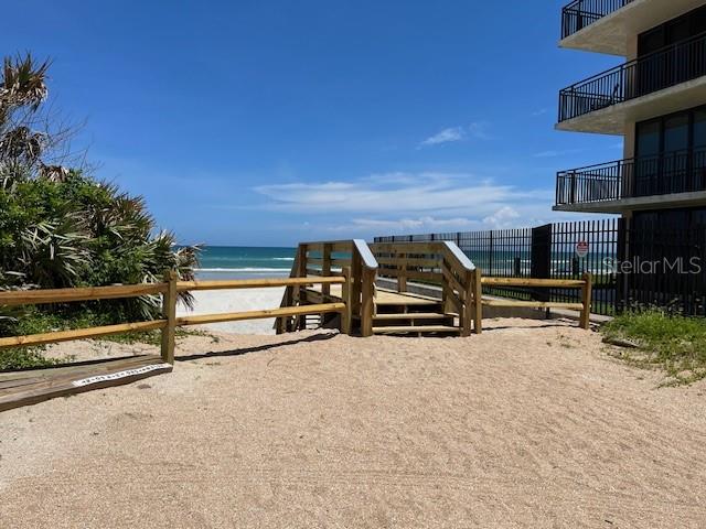 A wooden boardwalk leads to a sandy beach next to a multi-story residential building — 4150 S ATLANTIC AVENUE UNIT 121B, NEW SMYRNA BEACH, FL