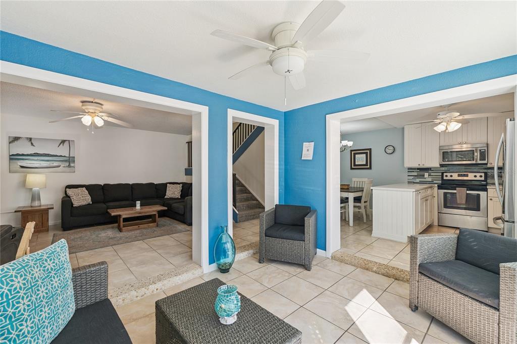 A living room with tile floors, blue walls, and openings to a kitchen and den — 4150 S ATLANTIC AVENUE UNIT 121B, NEW SMYRNA BEACH, FL