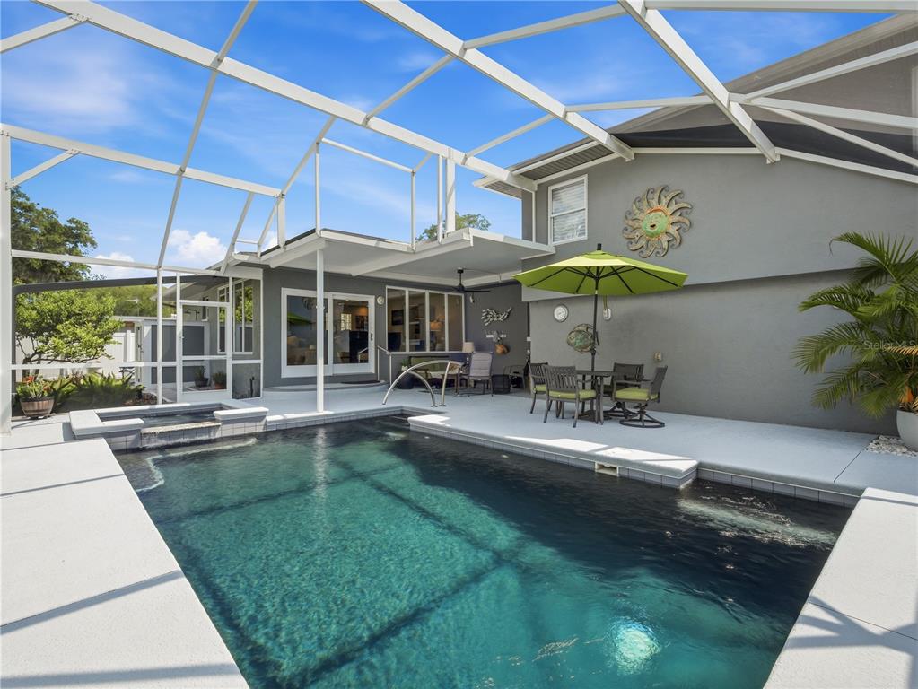 A swimming pool and spa are enclosed within a screened lanai behind a gray house — 1508 S RIVERSIDE DRIVE, NEW SMYRNA BEACH, FL