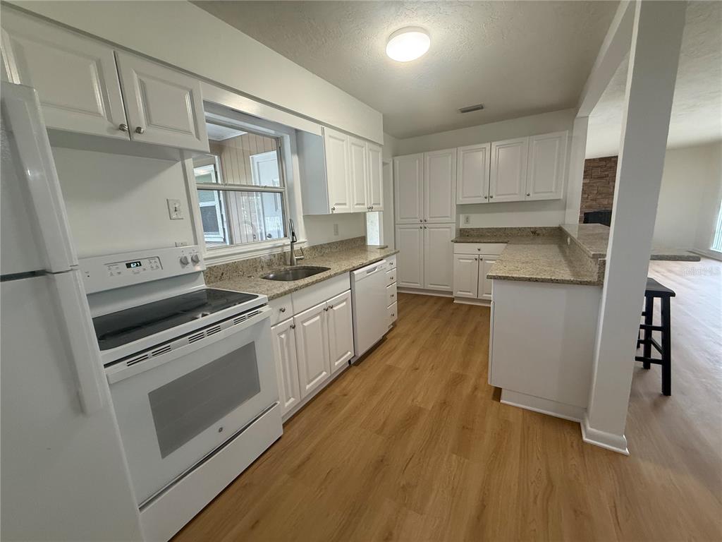 A kitchen features white cabinets, granite countertops, stainless steel appliances, and light wood-look flooring — 2588 COLORADO STREET, SARASOTA, FL