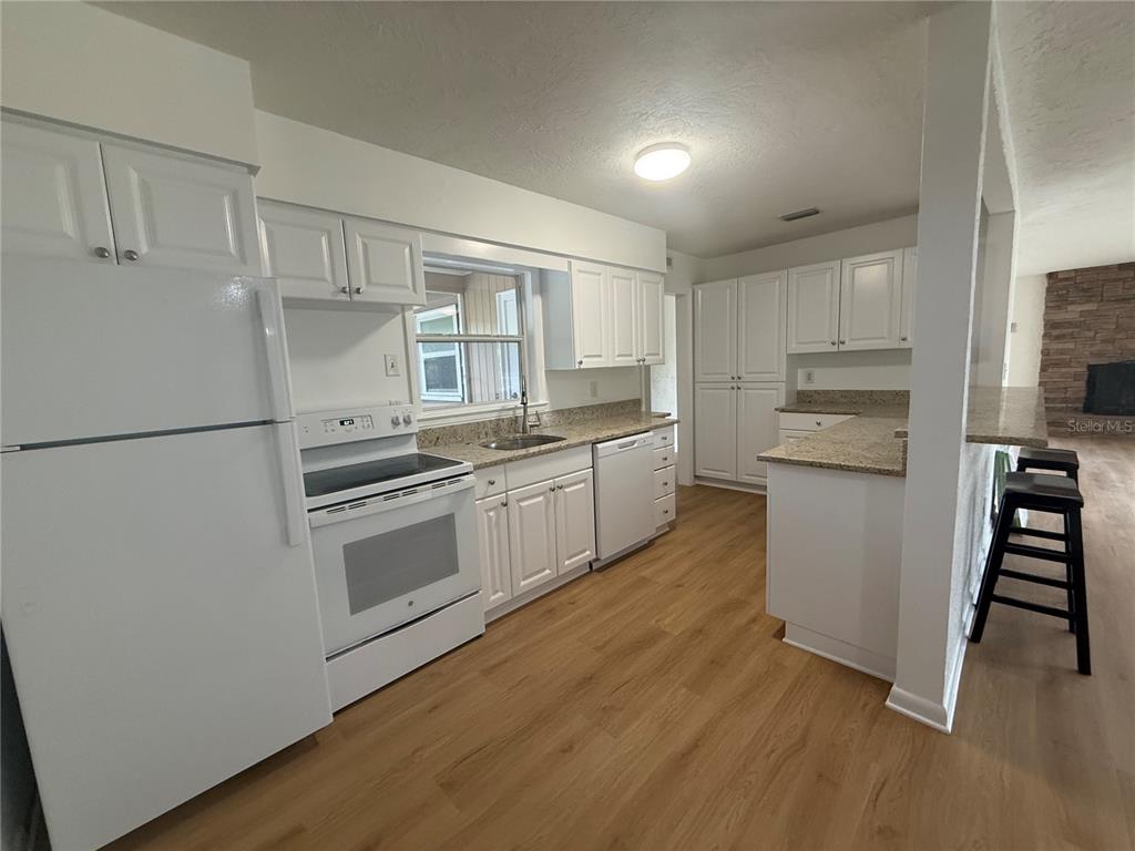 A kitchen features white cabinets, light countertops, stainless steel appliances, and light wood-look flooring — 2588 COLORADO STREET, SARASOTA, FL