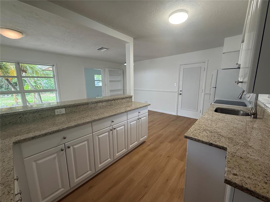A kitchen features white cabinets, granite countertops, and wood-look flooring, opening to an adjacent room — 2588 COLORADO STREET, SARASOTA, FL