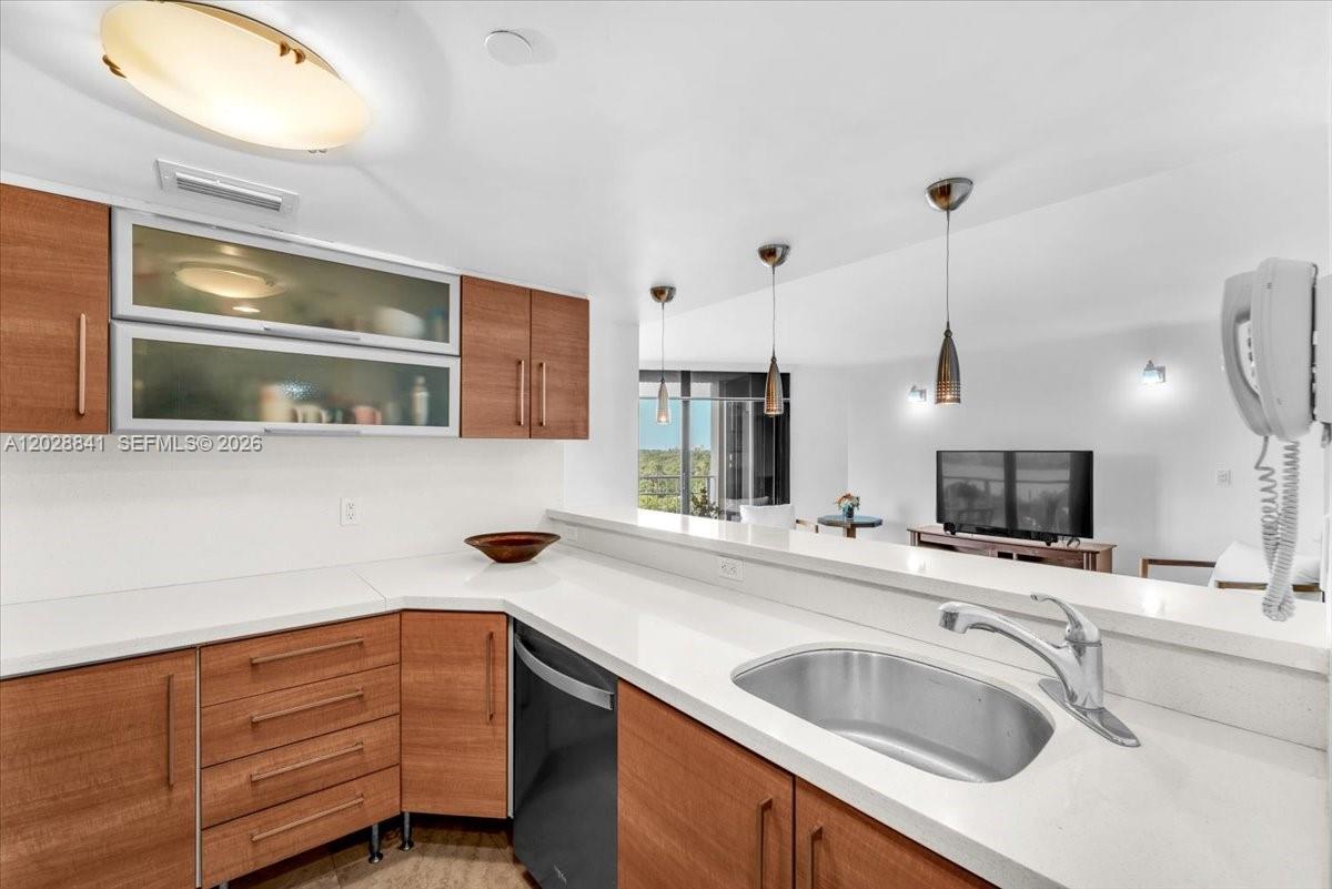 A kitchen features wood-toned cabinets, white countertops, and a view into the living area — 2000 Towerside Ter # 908, Miami FL 33138, MIAMI, FL