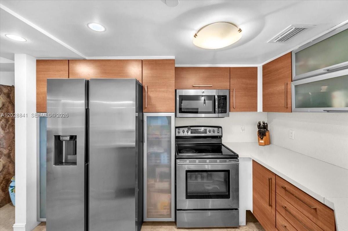 A kitchen features wood-toned cabinets, stainless steel appliances, and white countertops — 2000 Towerside Ter # 908, Miami FL 33138, MIAMI, FL