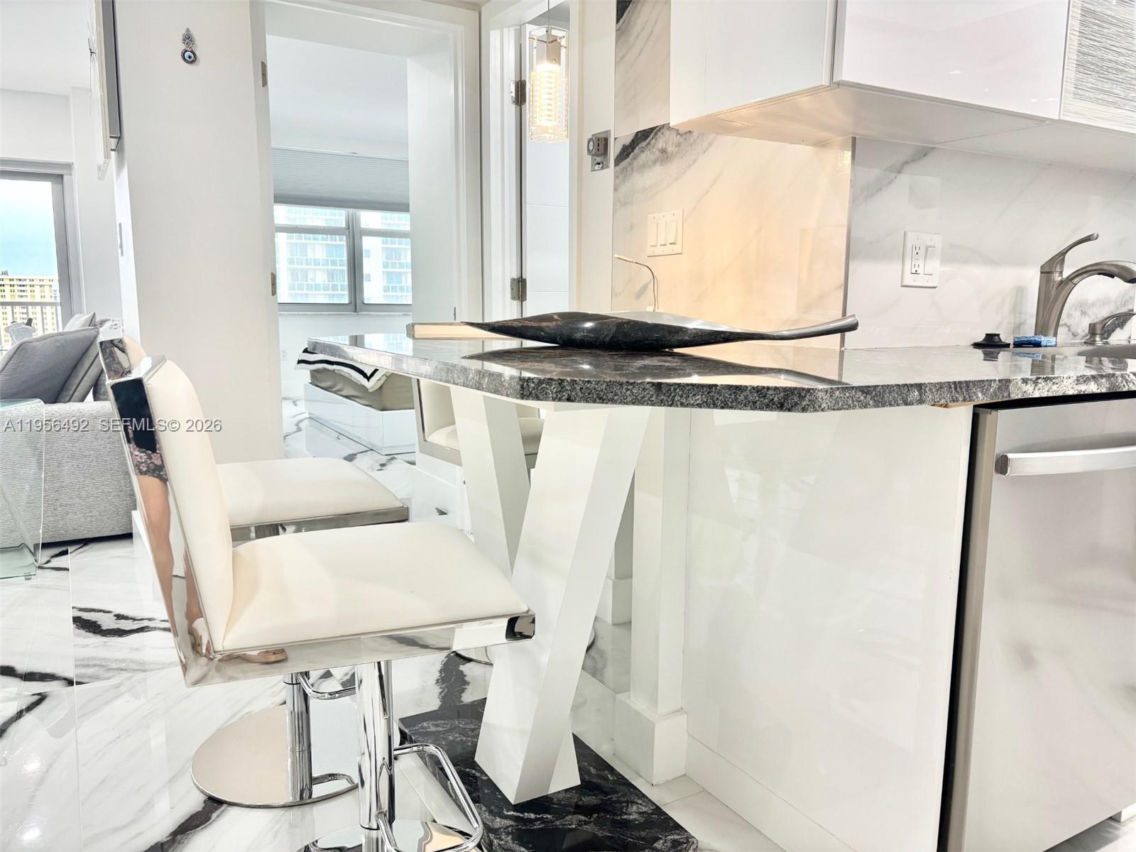 A modern kitchen island with a dark stone countertop and white base features bar stools — 1965 S Ocean Dr # 15B, Hallandale Beach FL 33009, HALLANDALE BEACH, FL