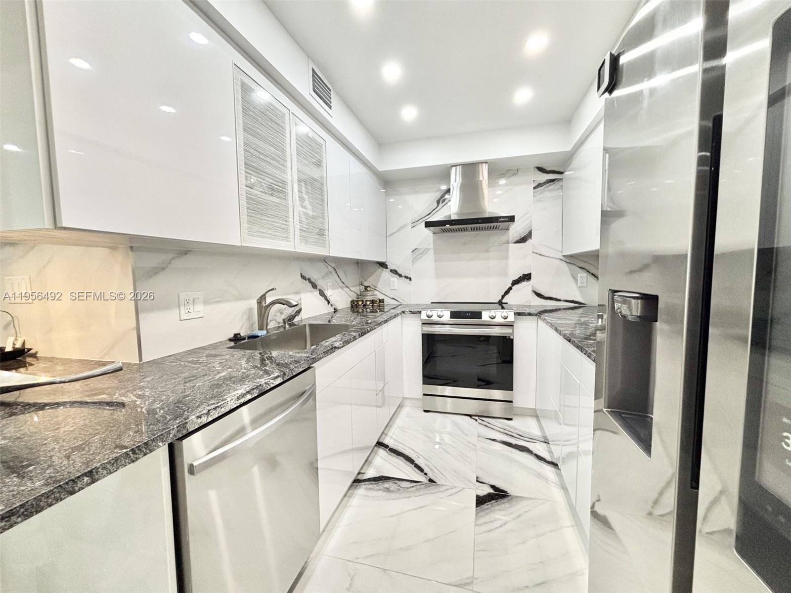 A modern galley kitchen features white glossy cabinets, marble-patterned flooring, and dark granite countertops — 1965 S Ocean Dr # 15B, Hallandale Beach FL 33009, HALLANDALE BEACH, FL