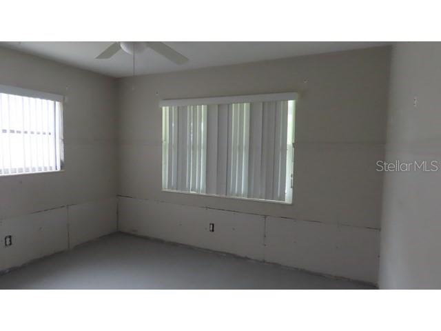 An unfinished room features bare drywall, vertical blinds on two windows, and a ceiling fan — 6060 62ND STREET N, ST PETERSBURG, FL