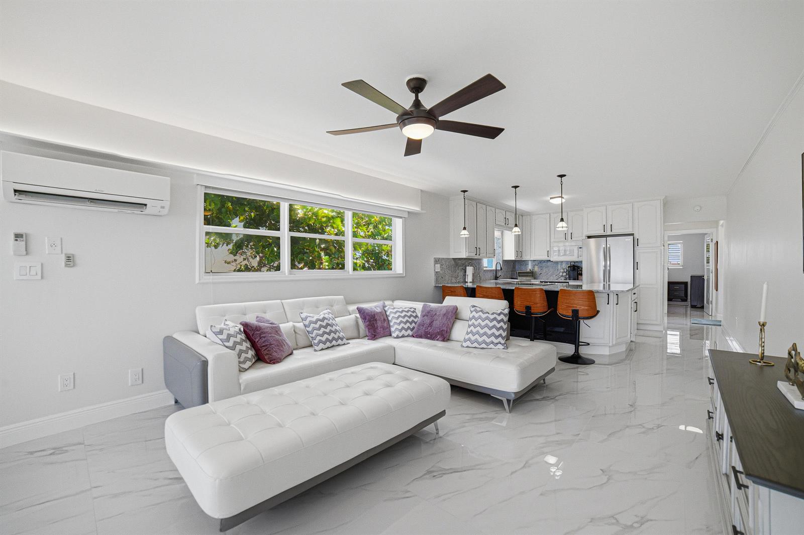 A modern open-concept living room and kitchen featuring white cabinetry, marble flooring, and a sectional — 8 Briny Avenue # 206, Pompano Beach FL 33062, POMPANO BEACH, FL