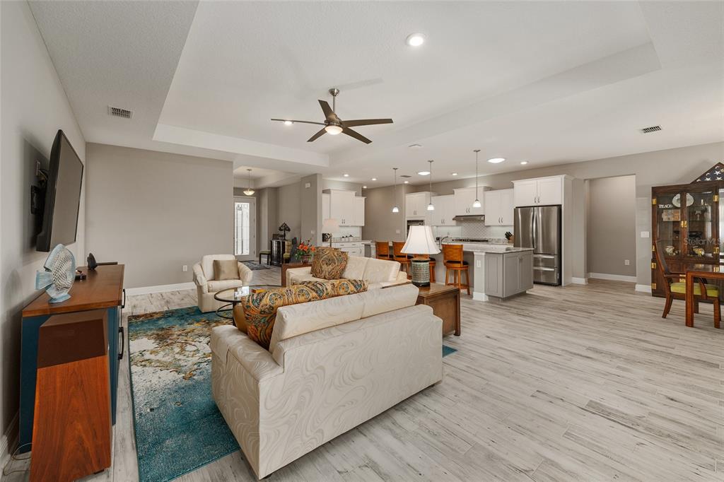 An open-concept living room and kitchen featuring light wood-look flooring and a tray ceiling — 8290 SW 92ND CIRCLE, OCALA, FL