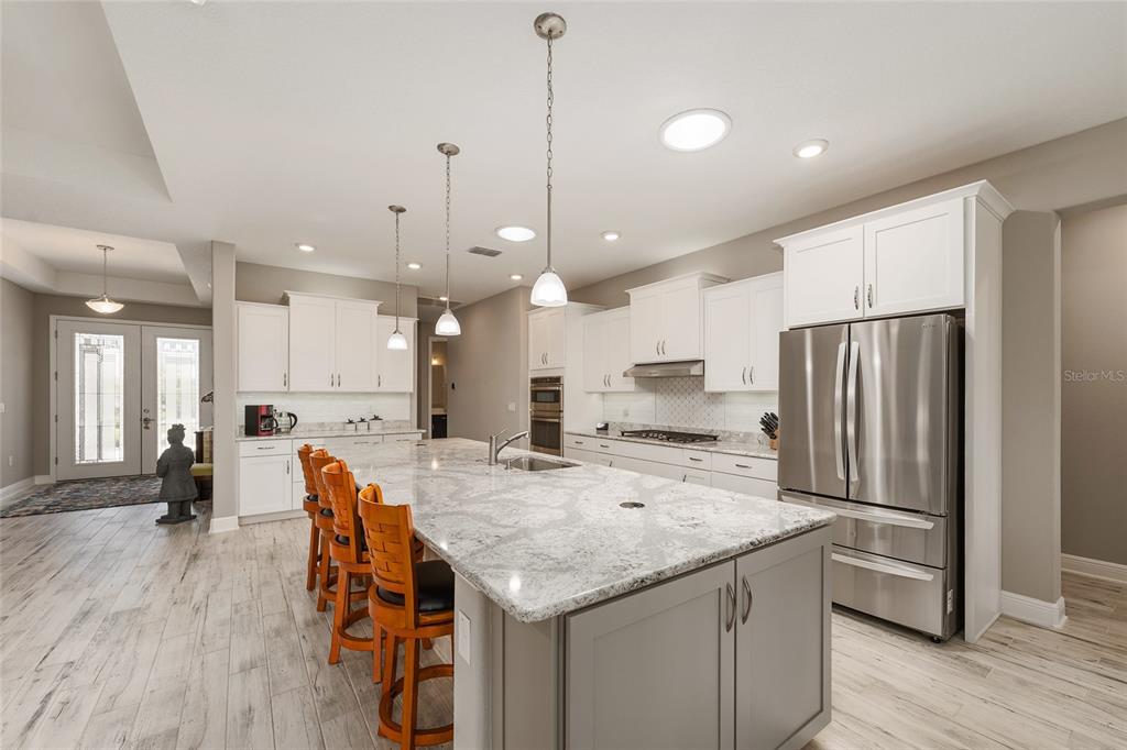 A kitchen features a large granite island, white cabinetry, stainless steel appliances, and wood-look flooring — 8290 SW 92ND CIRCLE, OCALA, FL