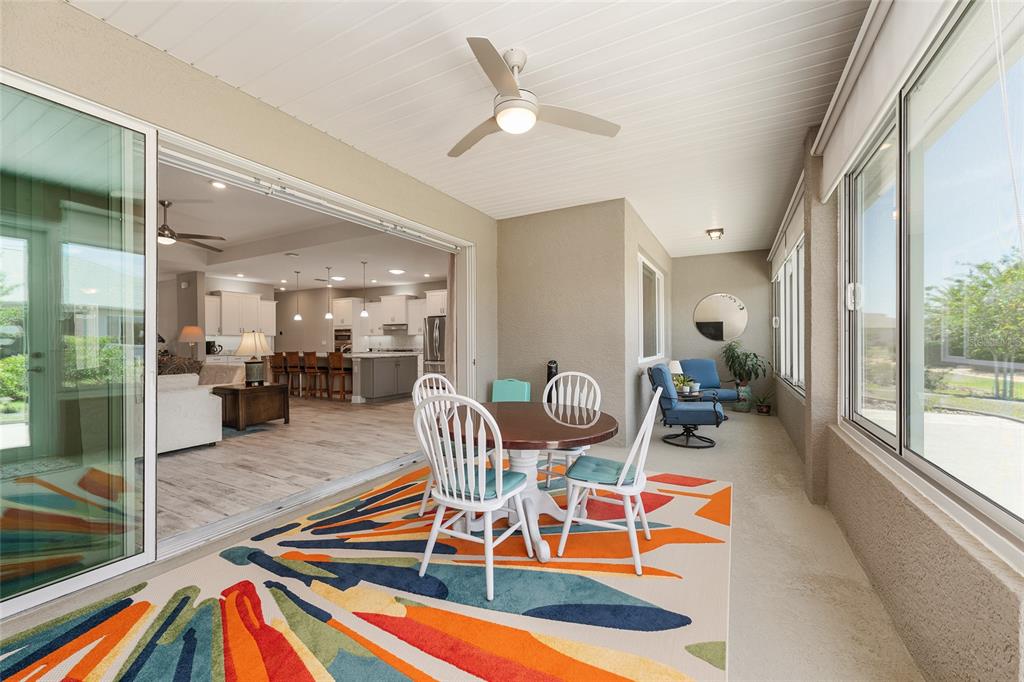 A covered patio features a colorful area rug, dining set, and sliding doors to the interior — 8290 SW 92ND CIRCLE, OCALA, FL
