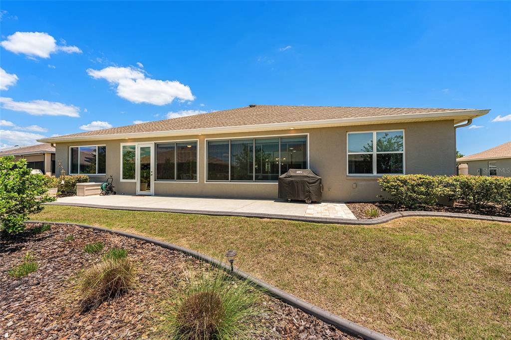 The exterior rear view of a house features a concrete patio, sliding glass doors, and windows — 8290 SW 92ND CIRCLE, OCALA, FL