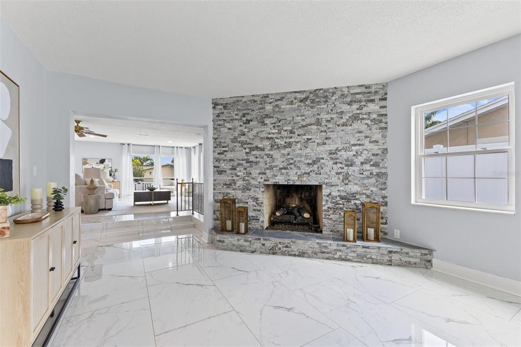 A living room features a stone fireplace, white marble-look tile flooring, and a sunken room beyond — 4000 14TH WAY NE, ST PETERSBURG, FL