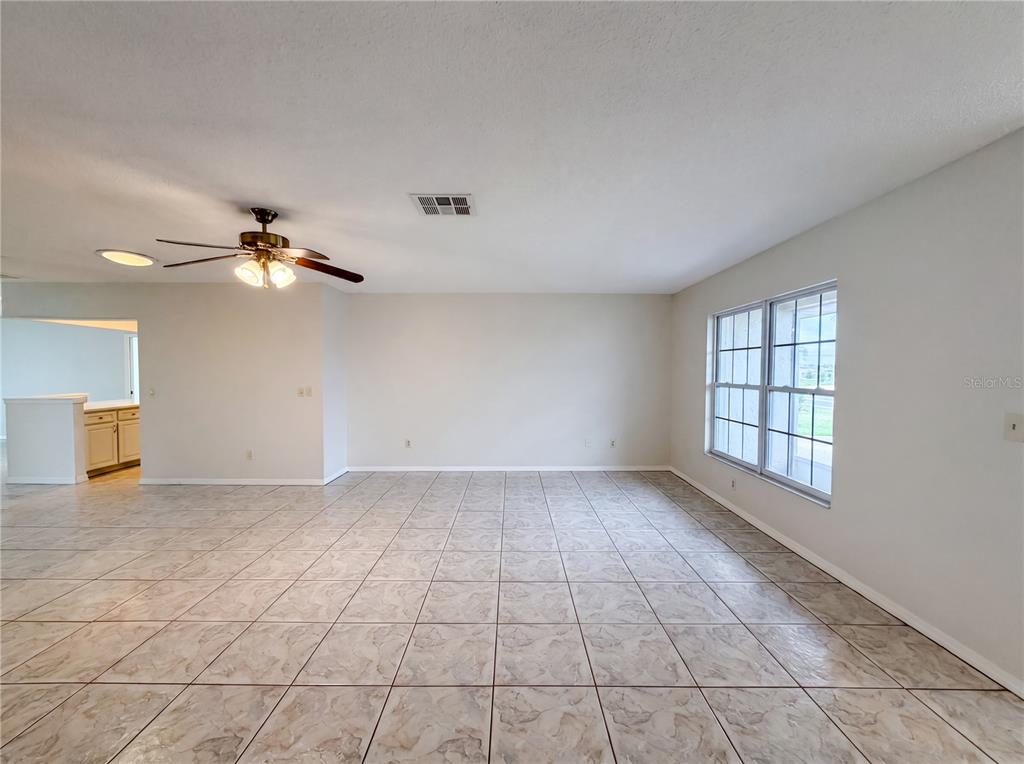 An empty room with light-colored tile flooring, a ceiling fan, and a large window — 1838 N PEBBLE BEACH BOULEVARD, SUN CITY CENTER, FL