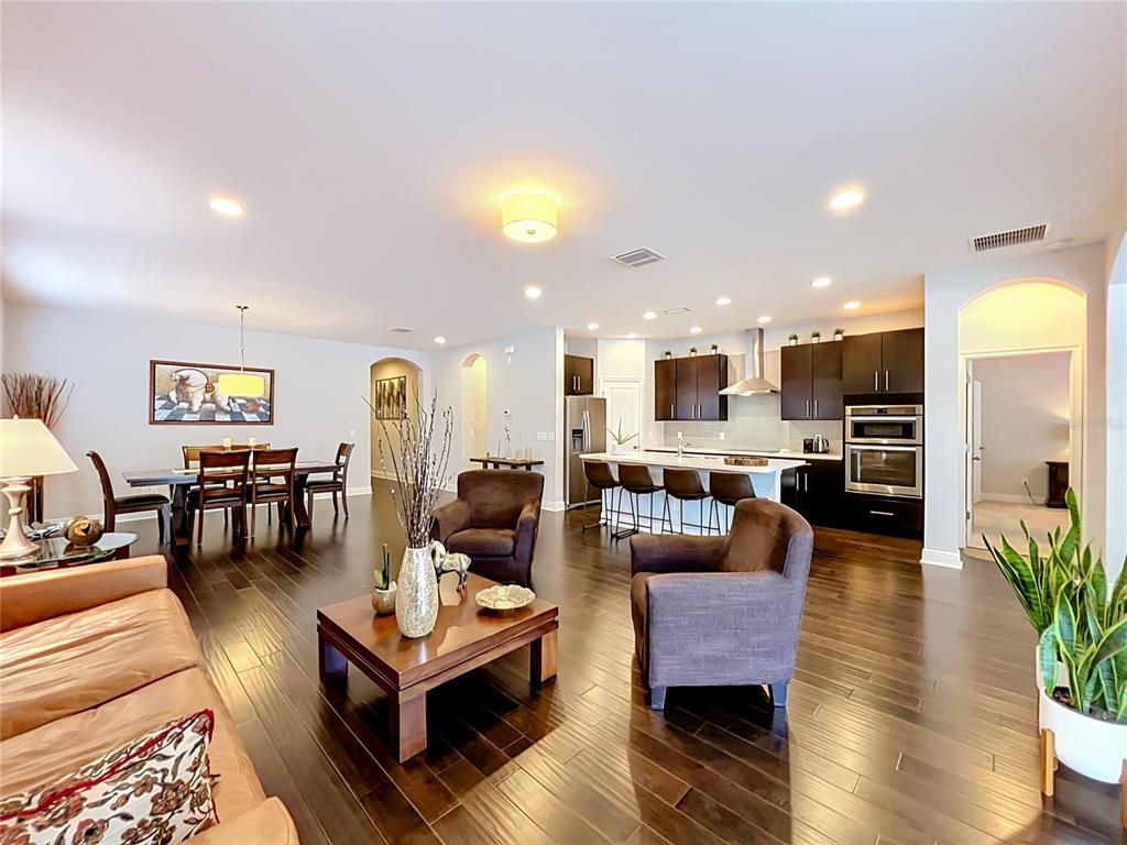 An open-concept living and dining area features dark wood floors, a kitchen island, and cabinetry — 7222 STILL POND LANE, WINDERMERE, FL