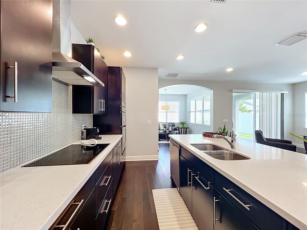A modern kitchen features dark cabinetry, white countertops, stainless steel appliances, and hardwood flooring — 7222 STILL POND LANE, WINDERMERE, FL