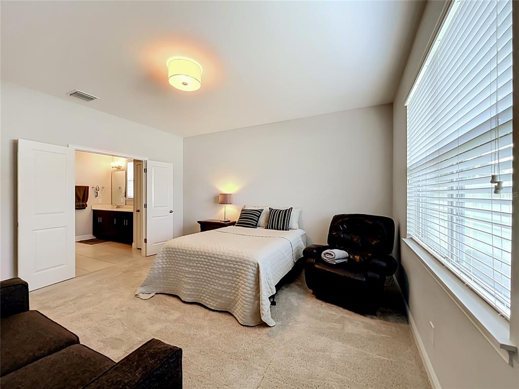 A bedroom features a bed, a dark leather recliner, and an open doorway to a bathroom — 7222 STILL POND LANE, WINDERMERE, FL