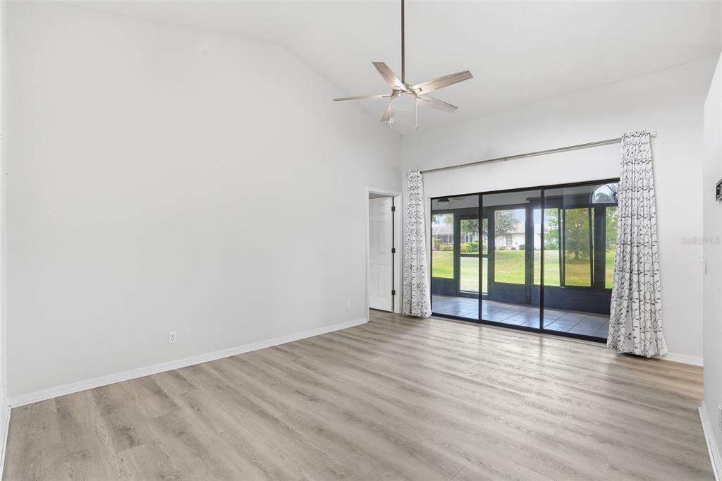A bright living room features light wood-look flooring, a ceiling fan, and sliding glass doors — 26070 DOLMAN COURT, PUNTA GORDA, FL