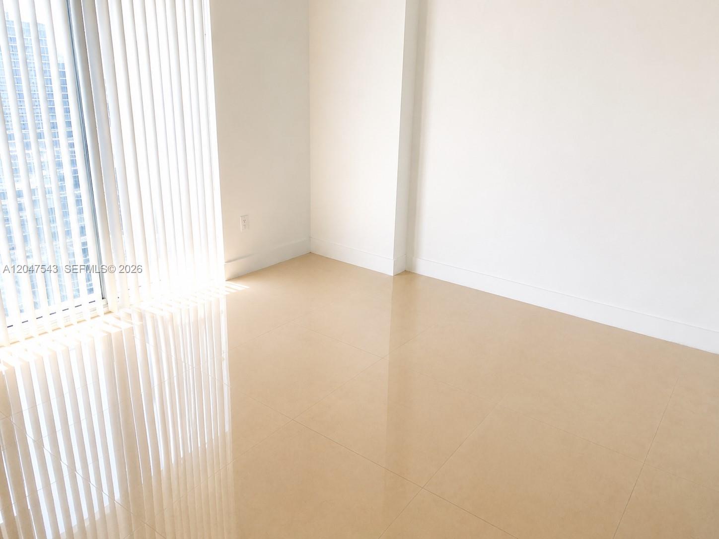 An empty room features light-colored tile flooring, white walls, and floor-to-ceiling vertical blinds — MIAMI, FL
