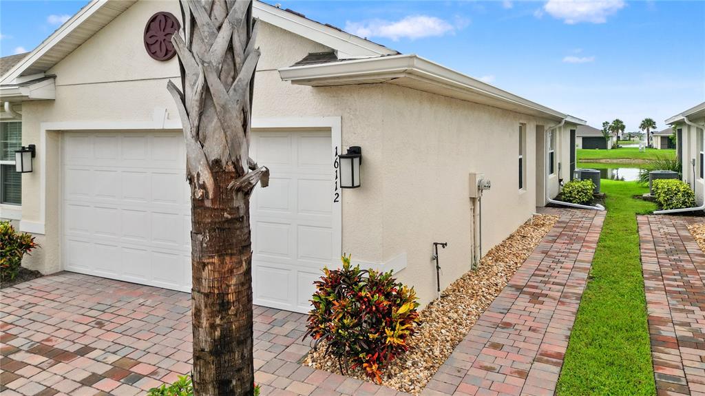 A beige house exterior features a two-car garage, a brick paver driveway, and landscaping — 16112 BRIDLE RIDGE STREET, PORT CHARLOTTE, FL