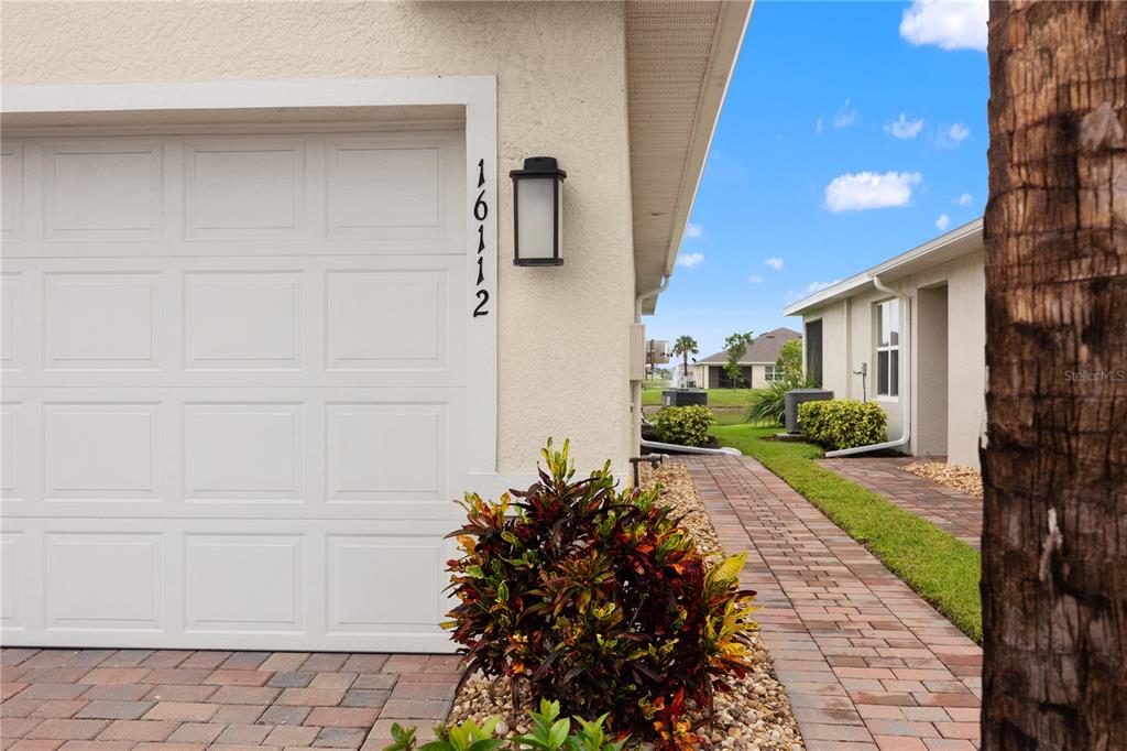 A white garage door with house numbers sits beside a brick walkway and landscaping — 16112 BRIDLE RIDGE STREET, PORT CHARLOTTE, FL