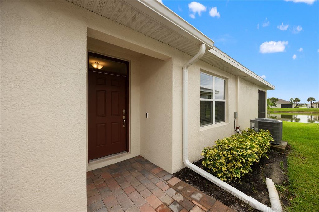 A brown front door sits under a covered entryway next to a window and landscaping — 16112 BRIDLE RIDGE STREET, PORT CHARLOTTE, FL