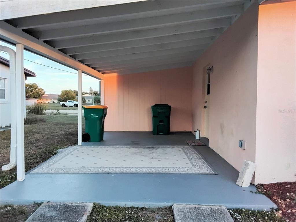 A covered concrete patio features a patterned area rug, two trash bins, and pink walls — 2440 ELKCAM BOULEVARD, PORT CHARLOTTE, FL
