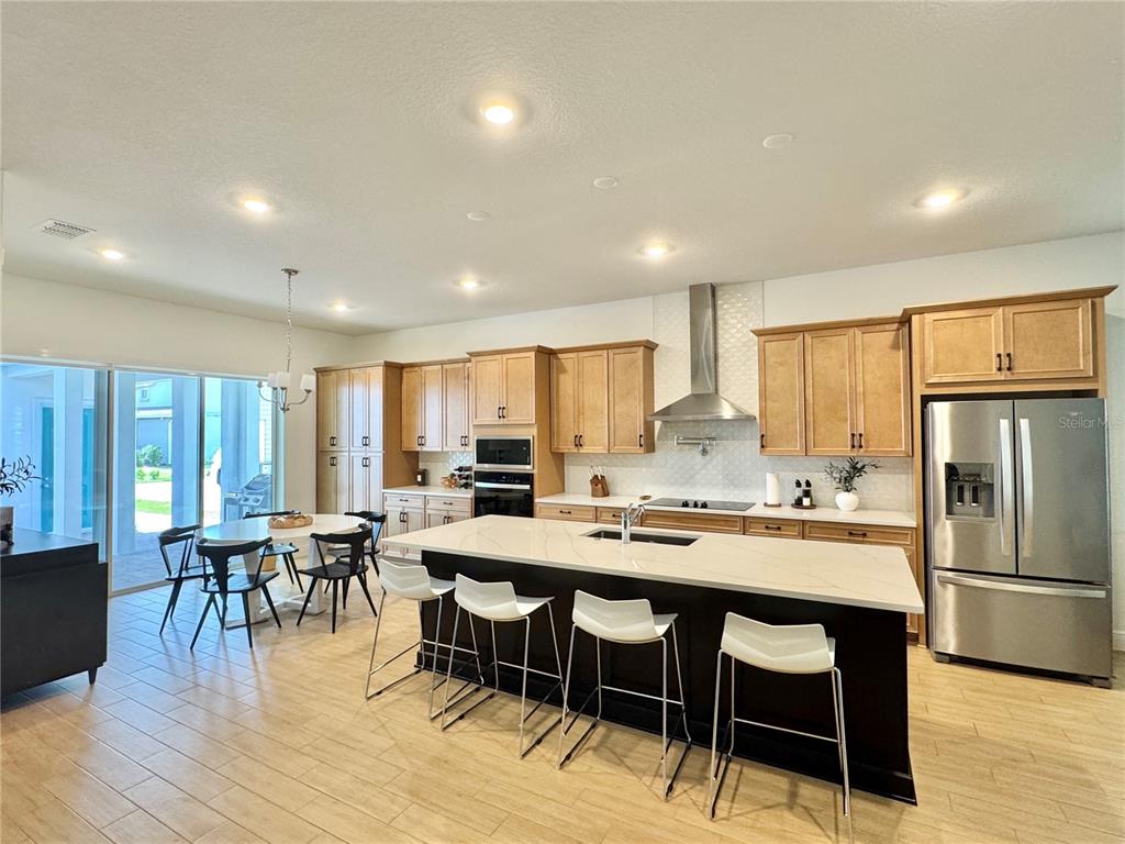 A modern kitchen features light wood cabinets, a dark island with seating, and stainless appliances — 13438 LEGGETT ALLEY, ORLANDO, FL